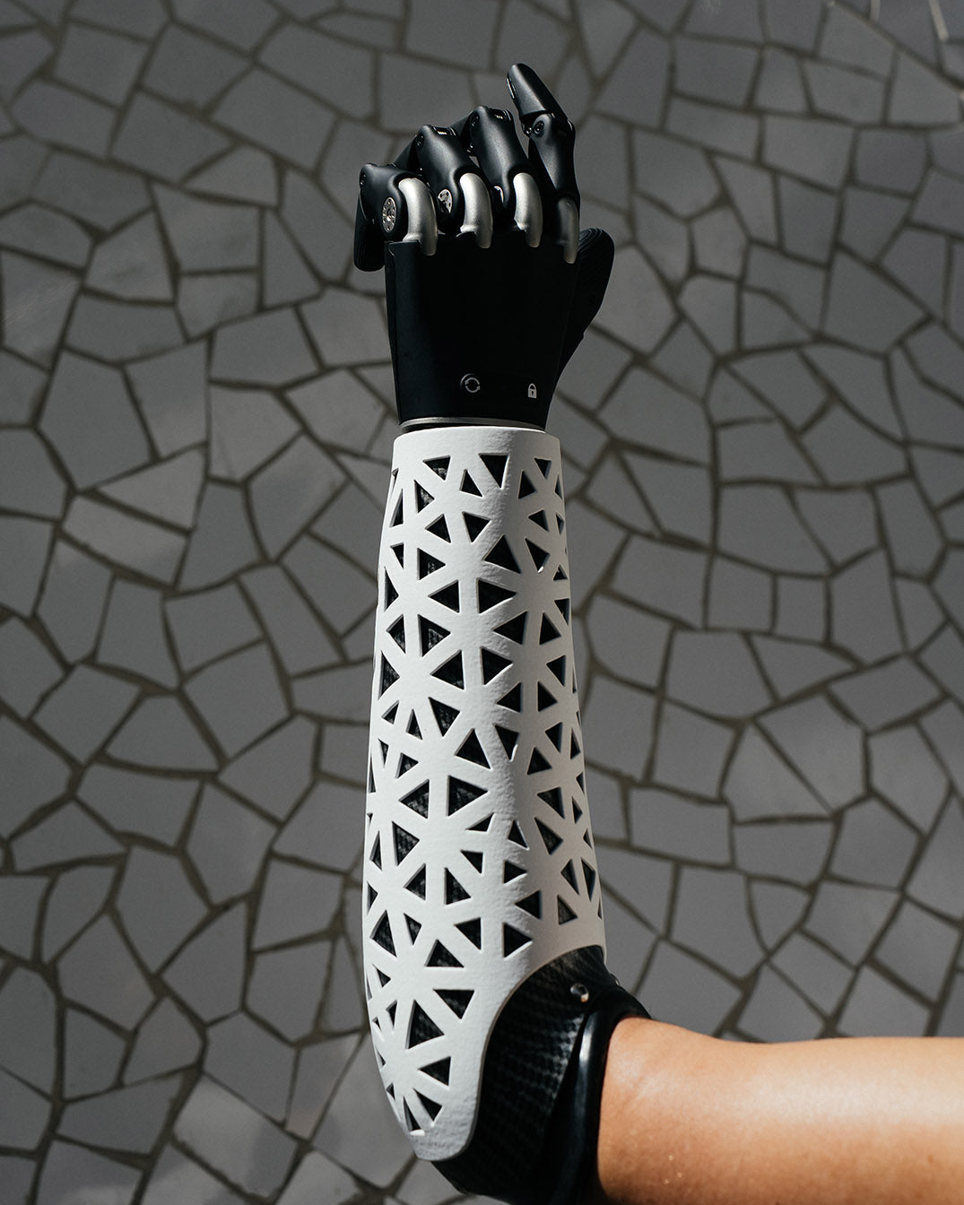 Prosthetic arm with black hand and a white geometric cover design on a gray mosaic background
