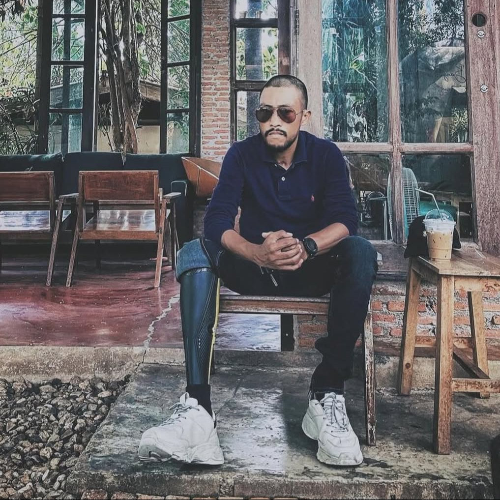 Man sitting in a rustic cafe with large windows and greenery outside